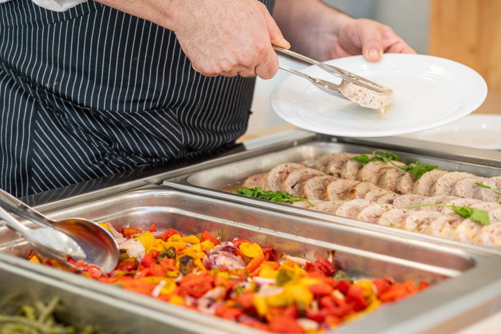 Lo chef serve gli antipasti caldi dal buffet del ristorante